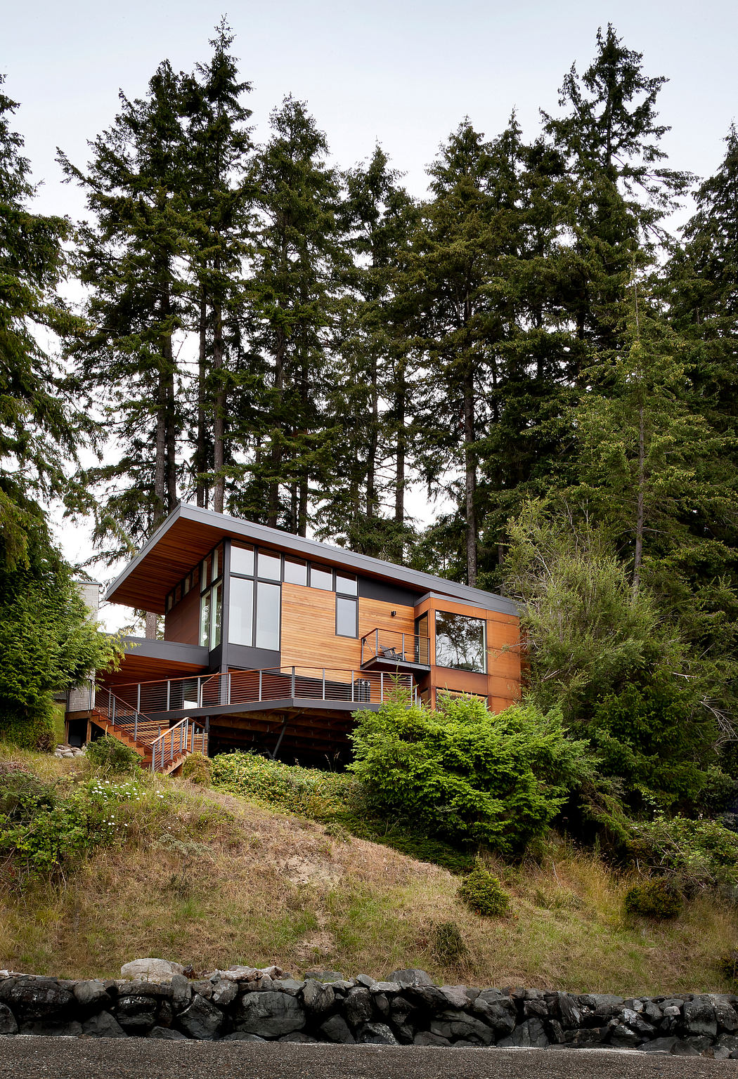 Modern cabin with large windows nestled among tall trees on a hillside.
