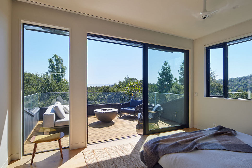 Modern bedroom with large windows opening to a balcony with a view of trees.