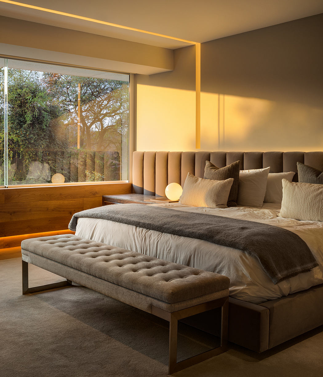Modern bedroom with large window, padded headboard, and bench at the foot of