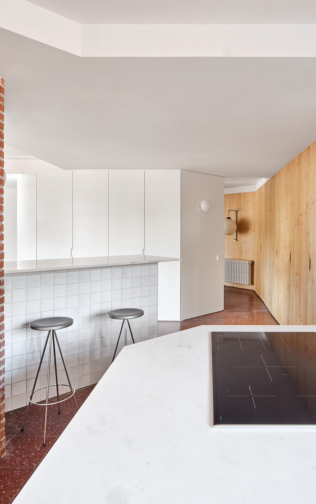 Modern kitchen with white cabinets, wood paneling, and bar stools.
