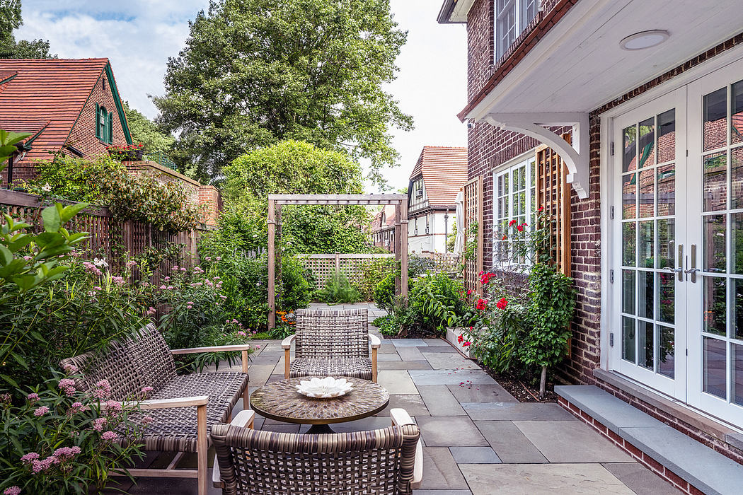 Cozy patio with wicker furniture and lush plants outside a brick house.