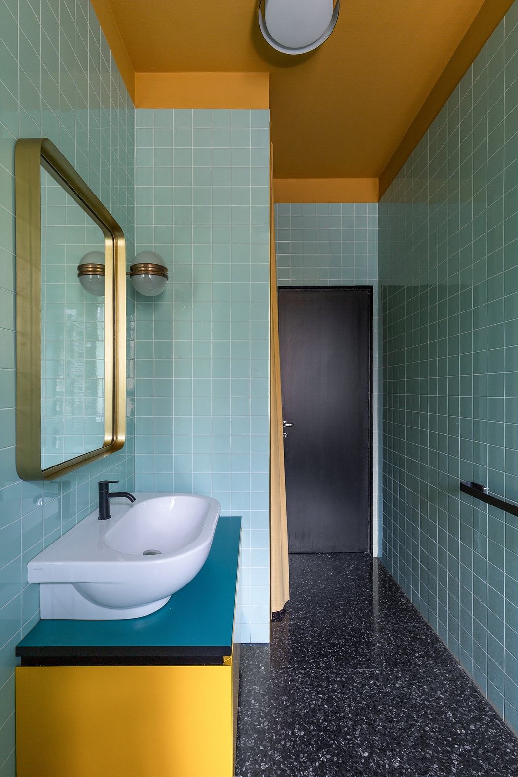 Modern bathroom with blue tiles, yellow walls, and a terrazzo floor.