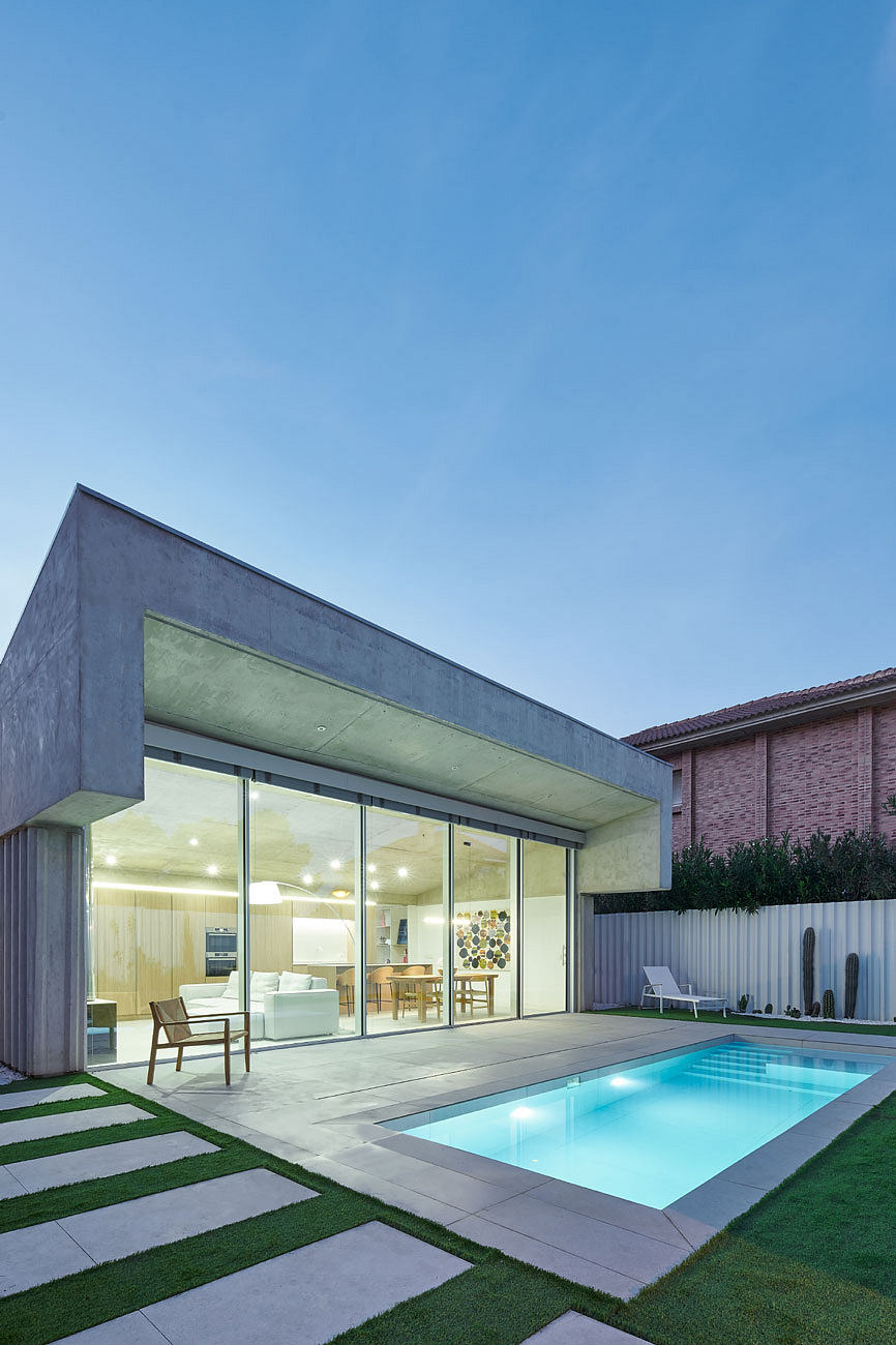 Minimalist house with large windows beside a pool at dusk.