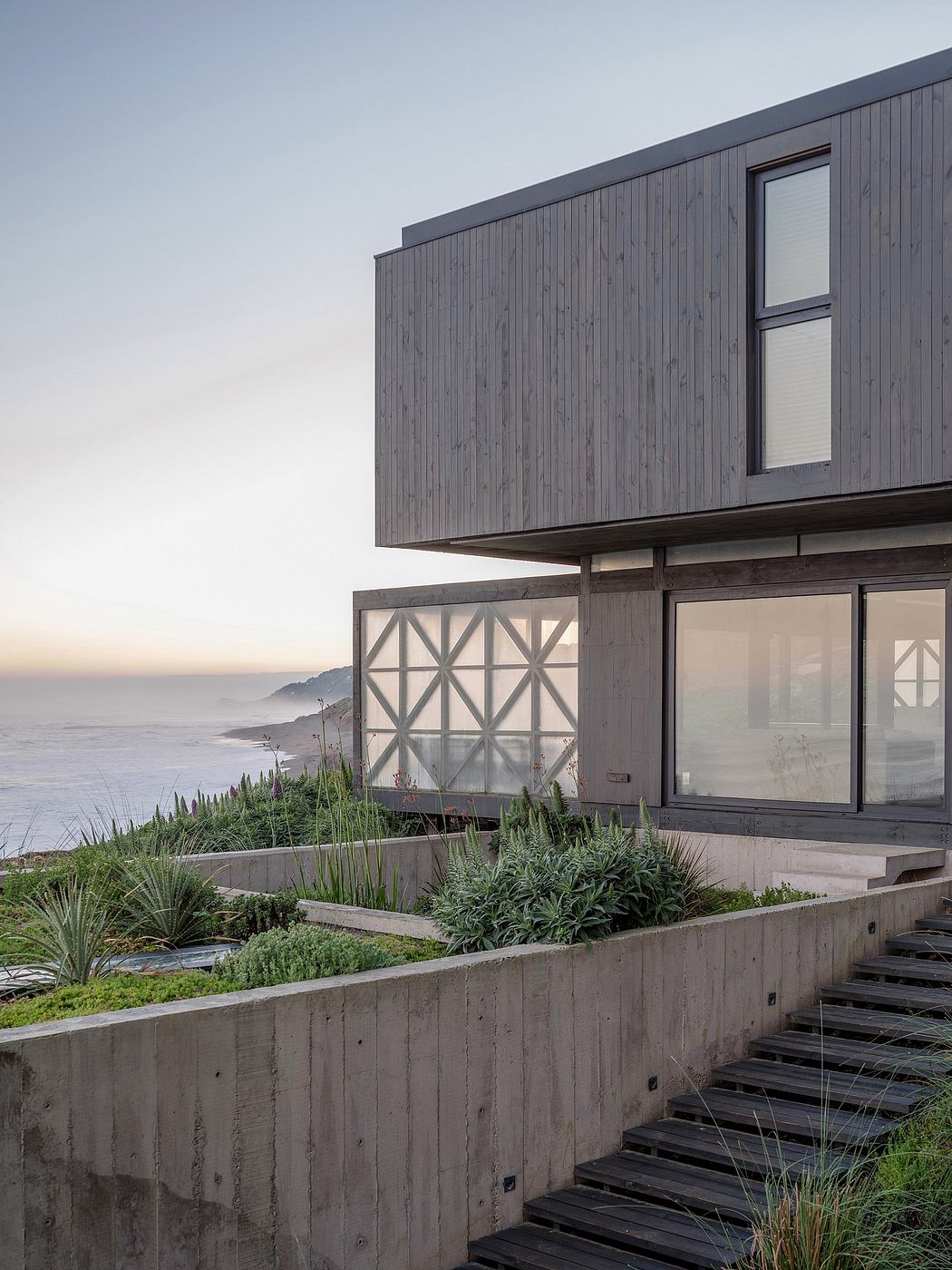 Modern beach house with wooden facade and concrete base at sunset.