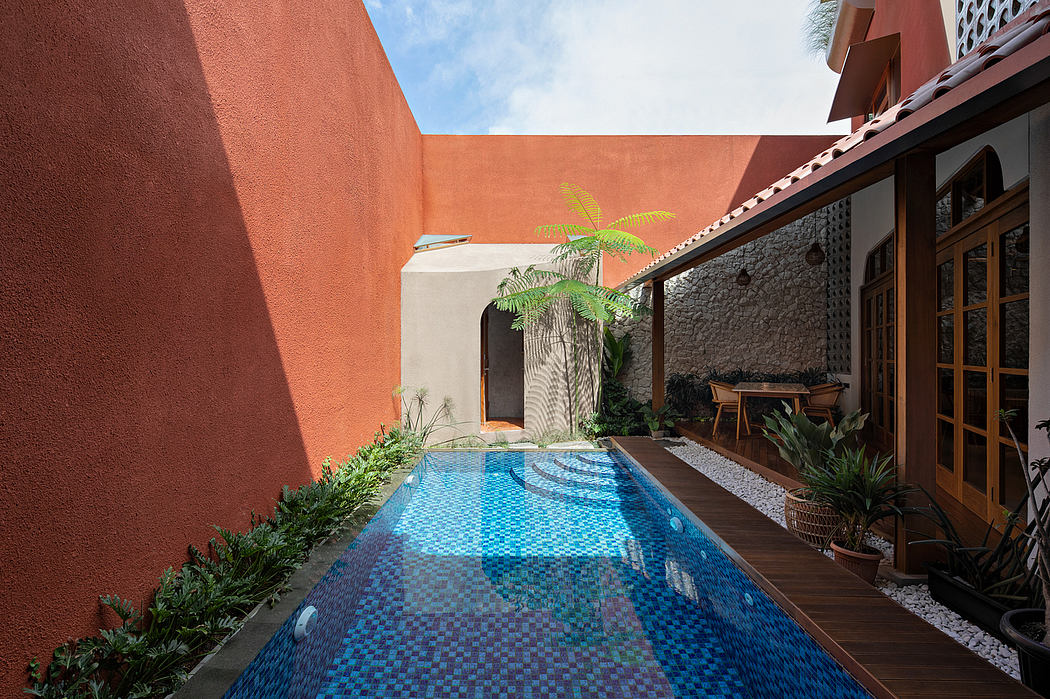 Narrow outdoor pool with mosaic tiles flanked by orange walls and a wooden deck