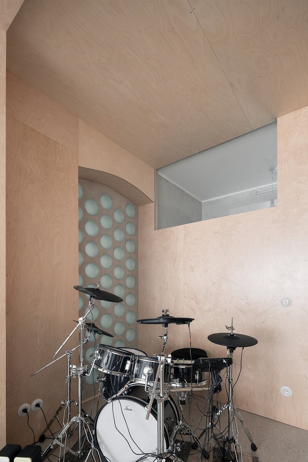 A drum set in a room with wooden walls and a circular glass-block window.