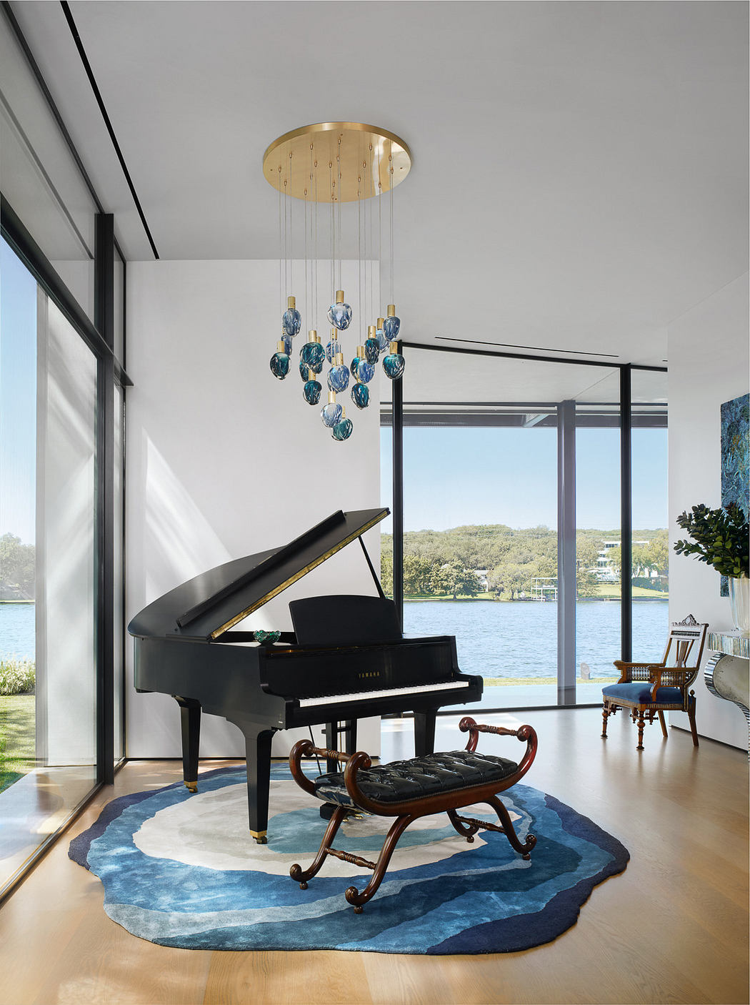Modern room with grand piano, blue chandelier, and lake view.