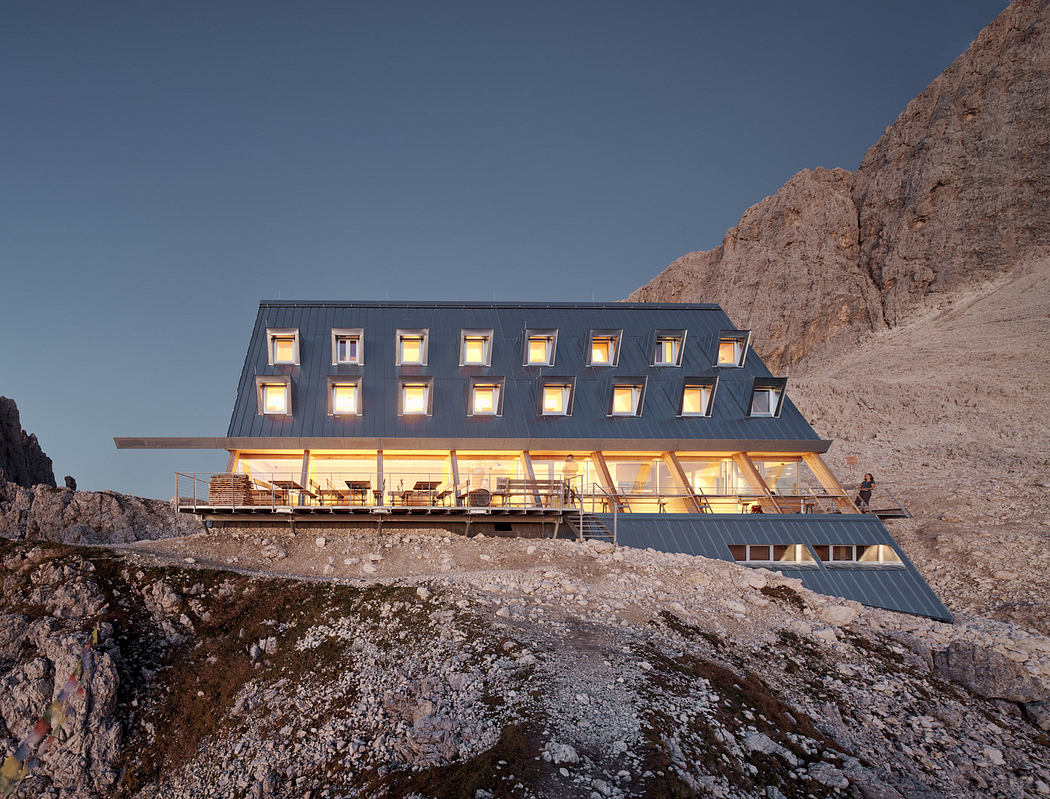 Modern mountain refuge hut at twilight with illuminated windows.