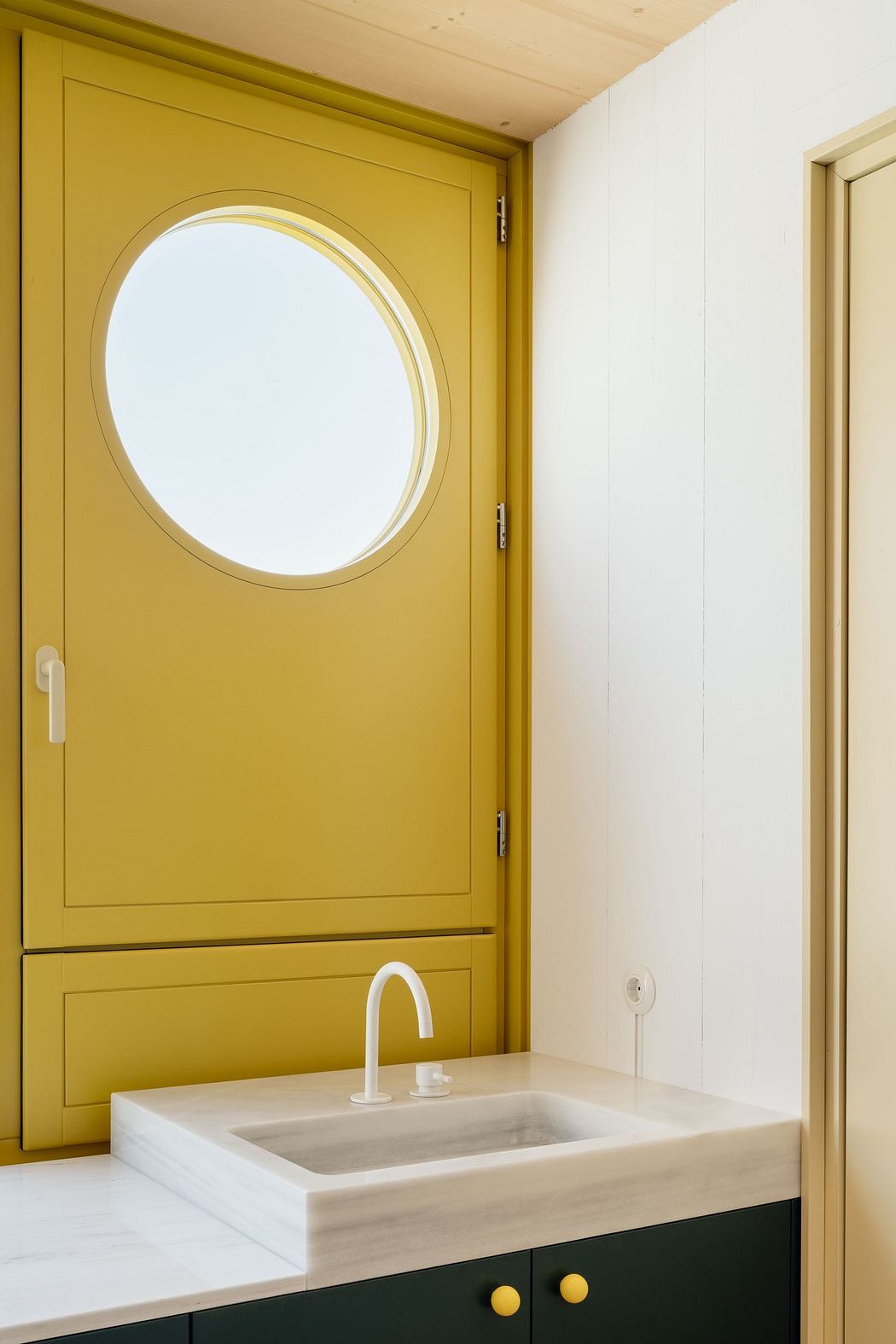 Minimalist bathroom with a mustard yellow door and circular mirror, white walls, and
