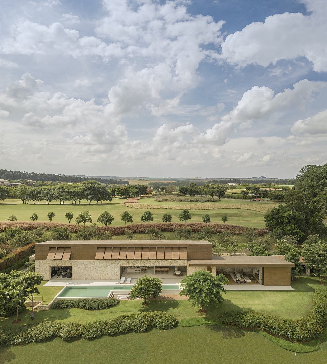 Modern house with a pool overlooking expansive green fields under a cloudy sky.