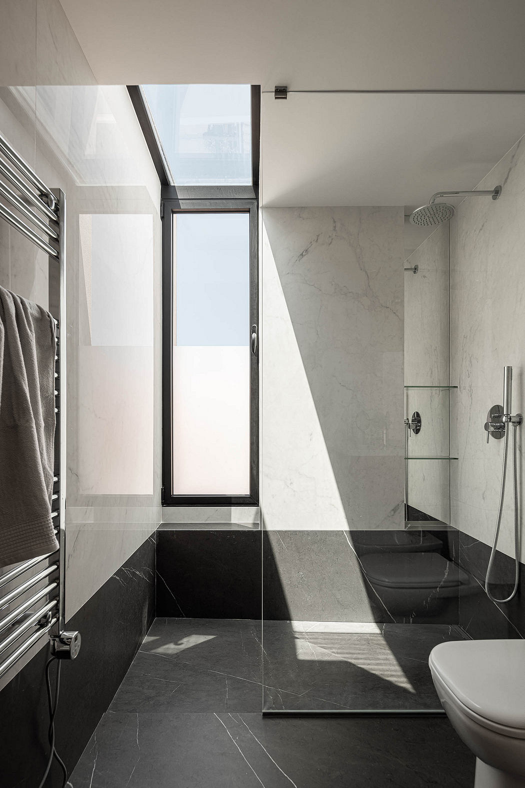Modern bathroom with black floor tiles, glass shower, and natural light.