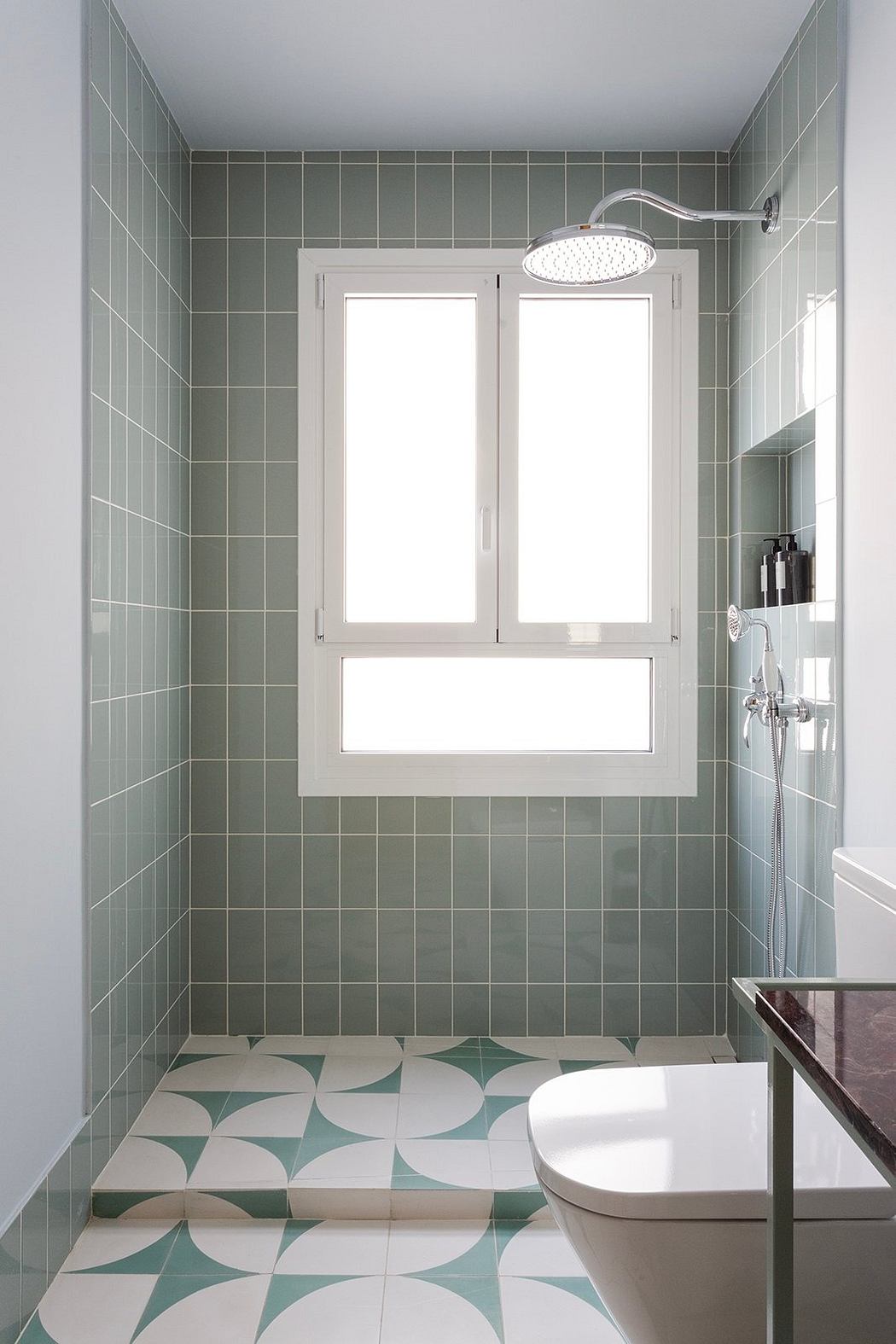 A minimalist bathroom with green tiled walls, patterned floor, and modern fixtures.