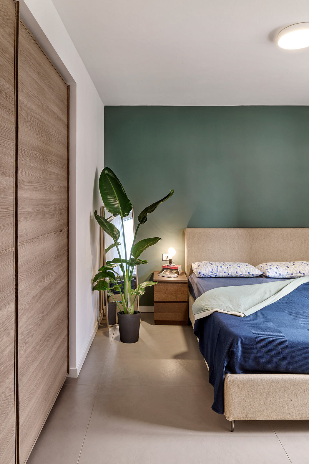 Contemporary bedroom with teal accent wall, large plant, and beige bed.