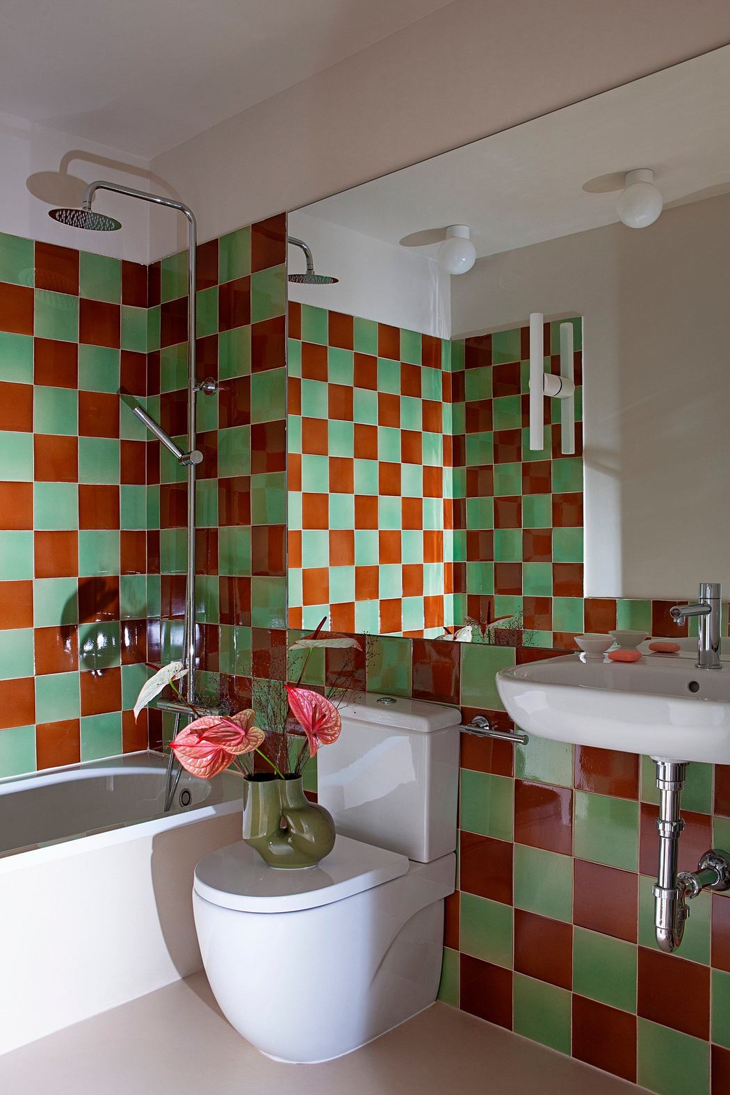 Modern bathroom with green and orange checkered tiles, white fixtures, and pink flowers