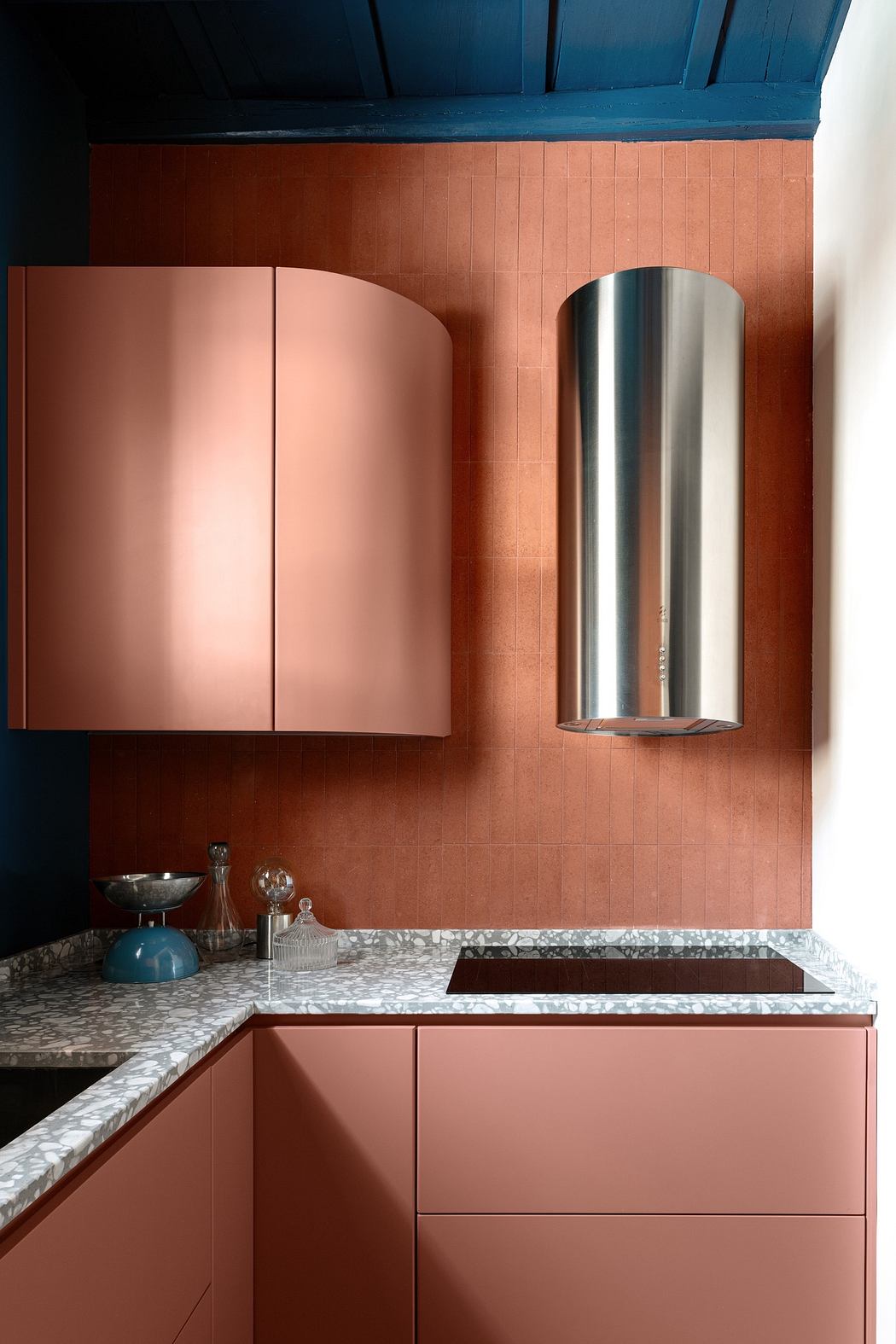 Modern kitchen with pink cabinets, terracotta walls, and blue ceiling.
