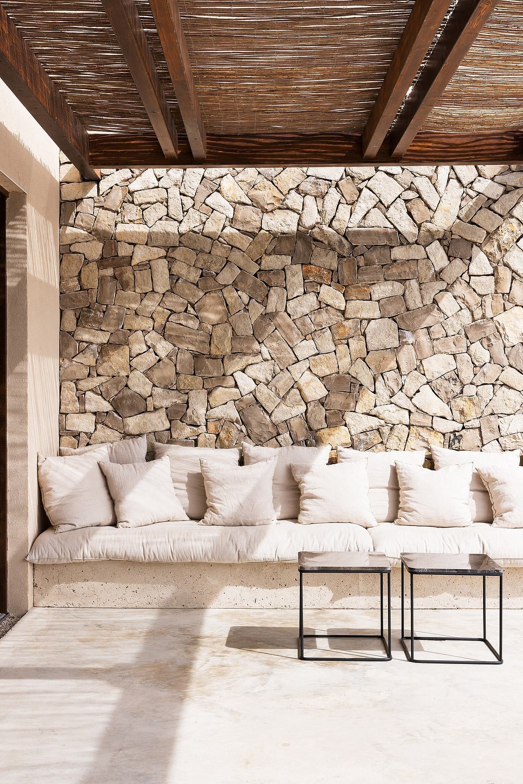 Outdoor lounge area with a stone wall, cushioned bench, and a wooden roof