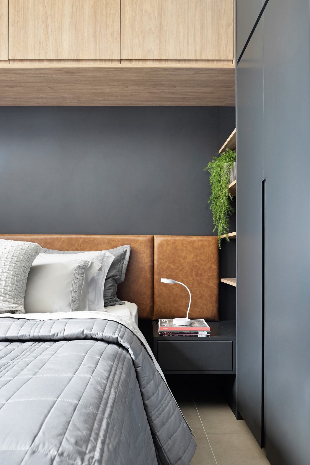 Contemporary bedroom with sleek grey bedding, tan headboard, and wooden accents.