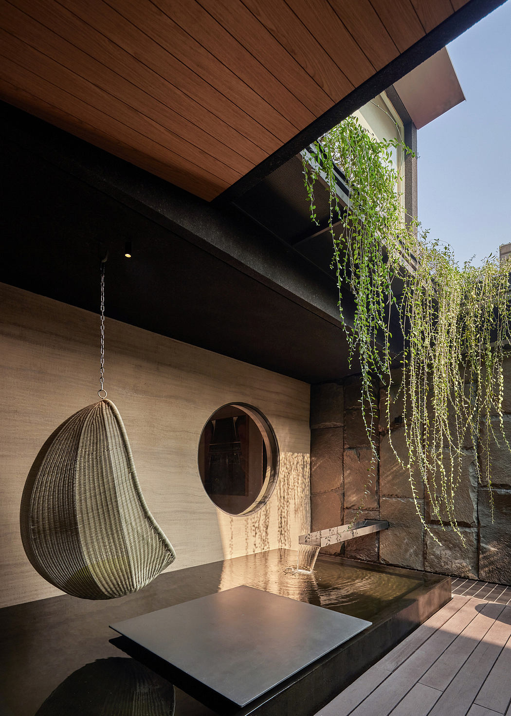 Modern outdoor patio with hanging chair, wooden decking, and cascading plants.