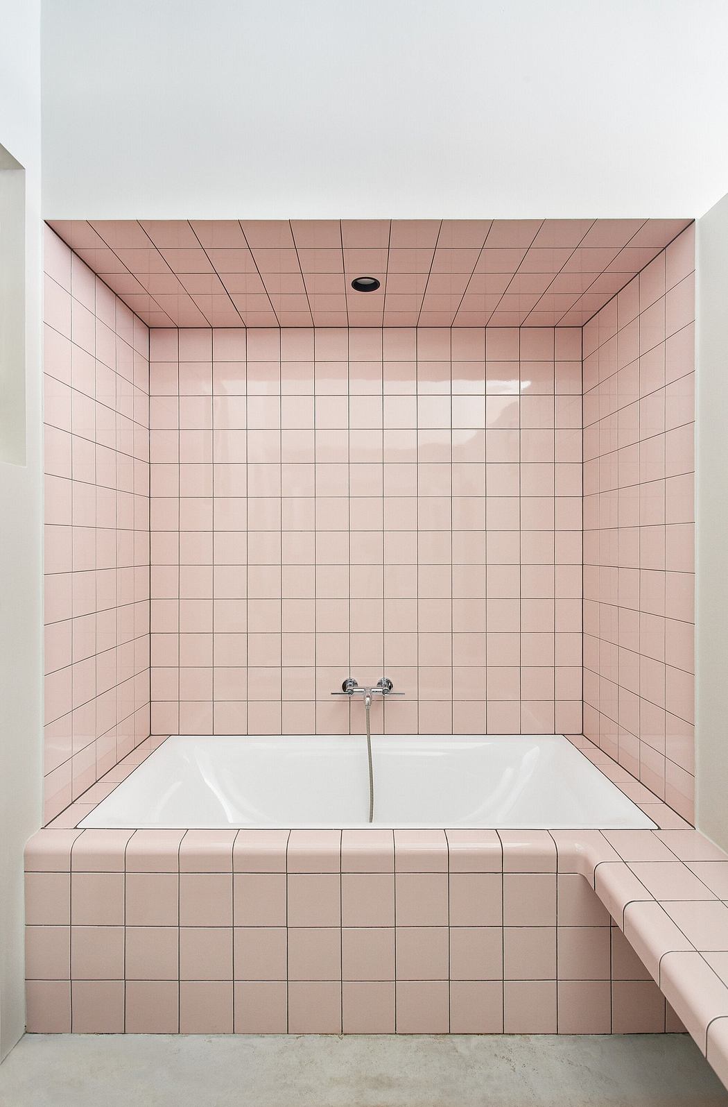 A pink-tiled bathroom with a white corner bathtub.