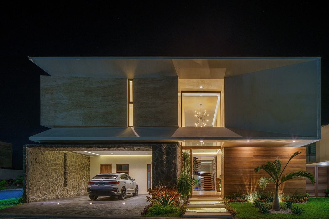 Modern two-story house at night with illuminated facade and car parked outside.