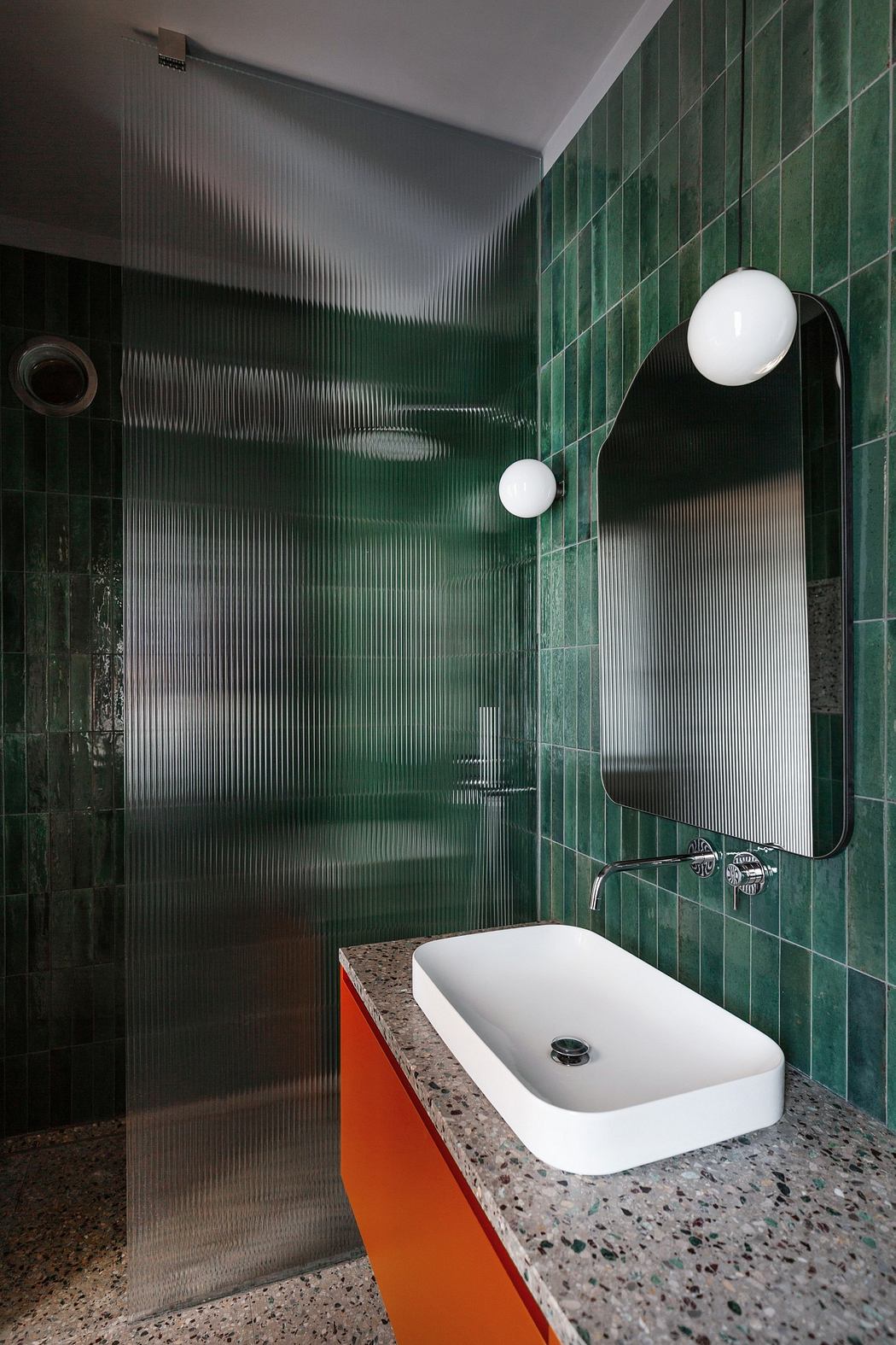 Modern bathroom with green tiles, glass partition, and an orange cabinet.