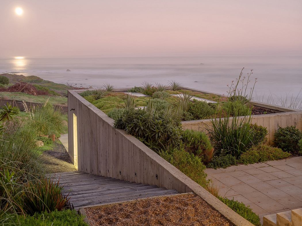 Coastal garden at twilight with wooden walkway and sea view.