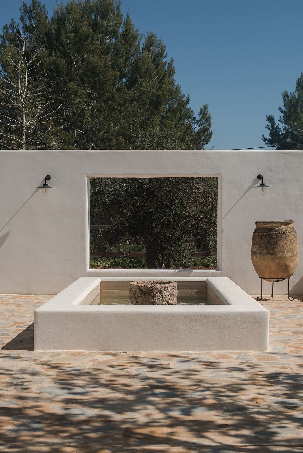 Minimalist courtyard with wall cutout framing nature, and clay pot decor.