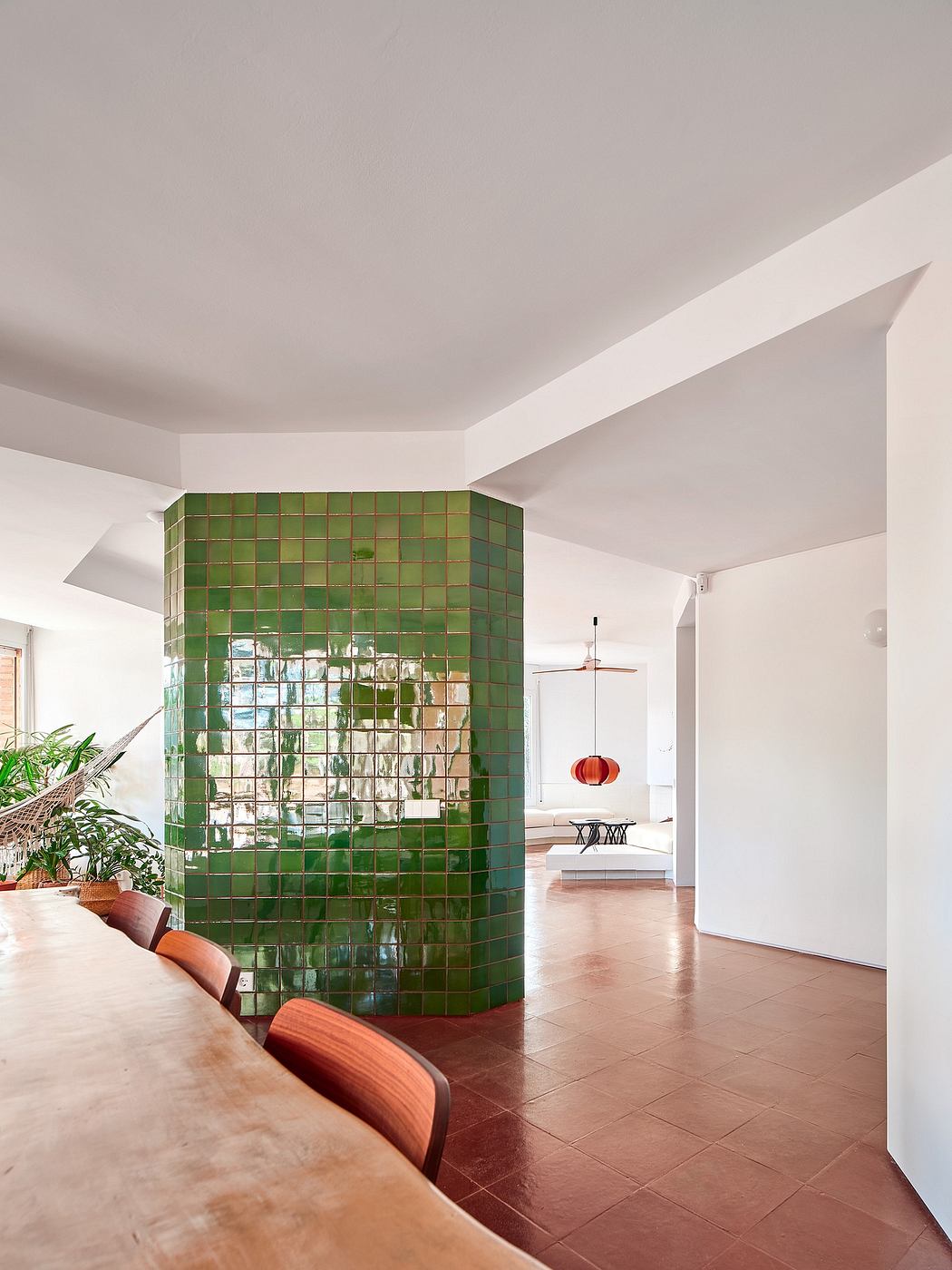 Modern room with a green tiled column, wooden table, and hanging chair in the