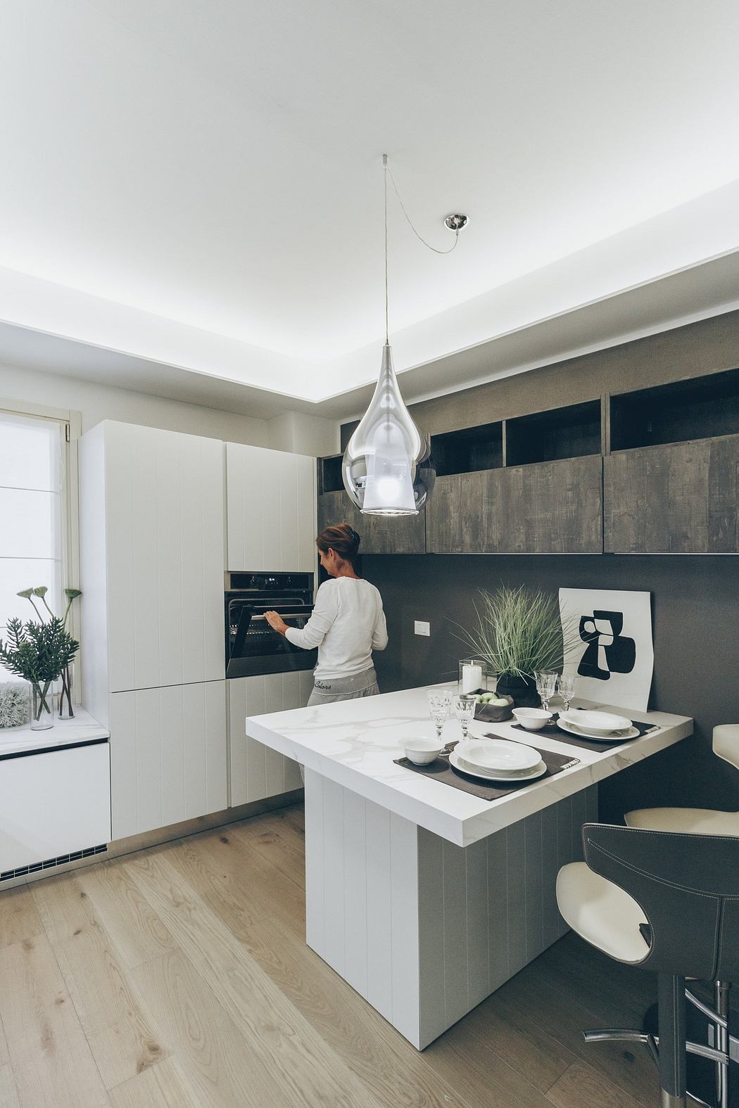Contemporary kitchen with pendant light, white counters, and person cooking.