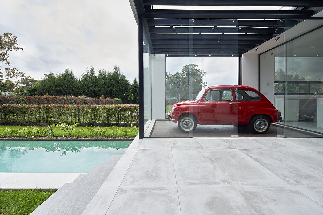 Modern home with glass walls, a red vintage car parked inside, and a pool