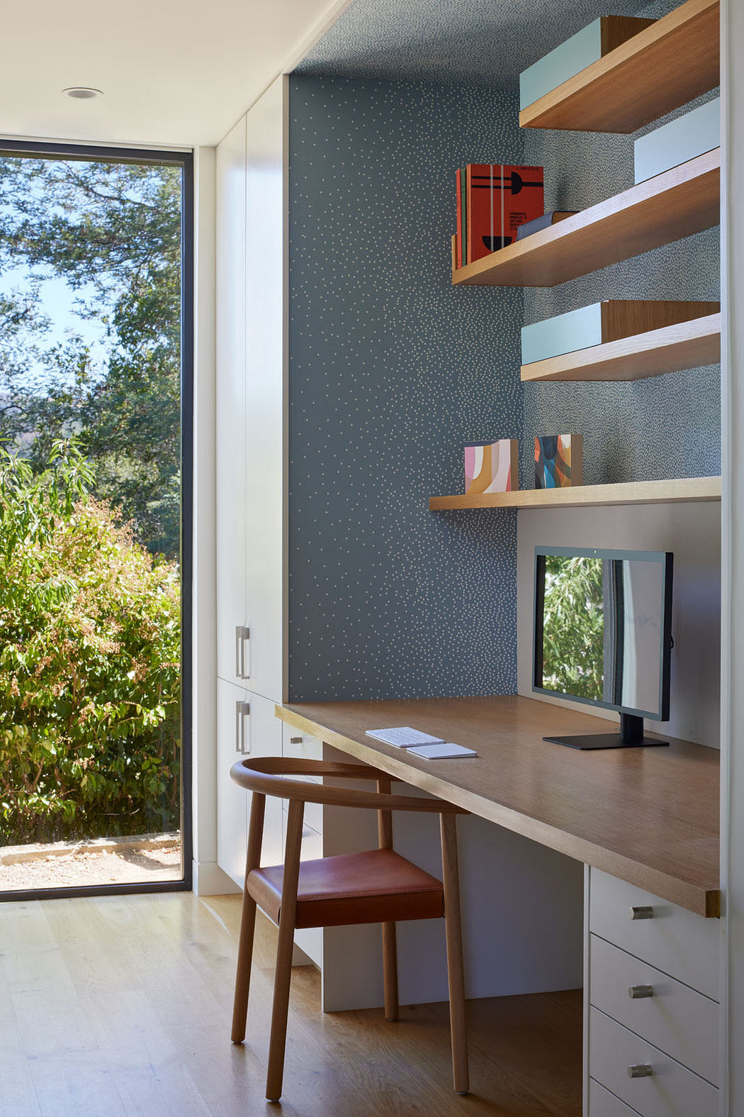 Contemporary home office with floating shelves and patterned wallpaper.