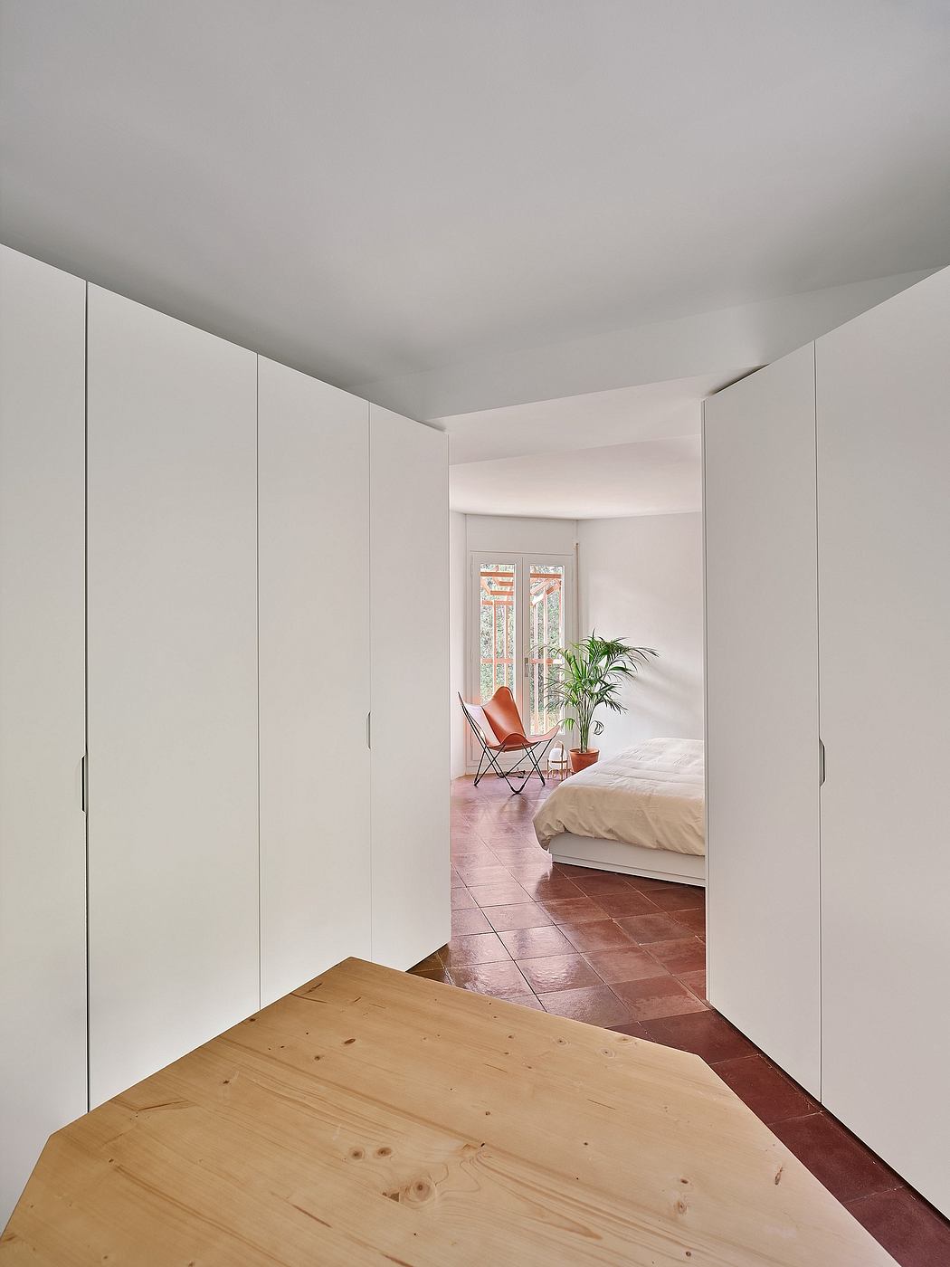 Minimalist hallway with white walls leading to a bedroom with a red chair.