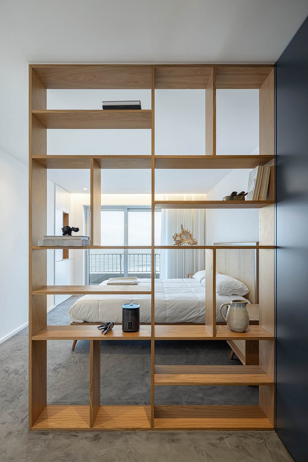 Minimalist wooden shelving unit doubling as a room divider with a bed in the