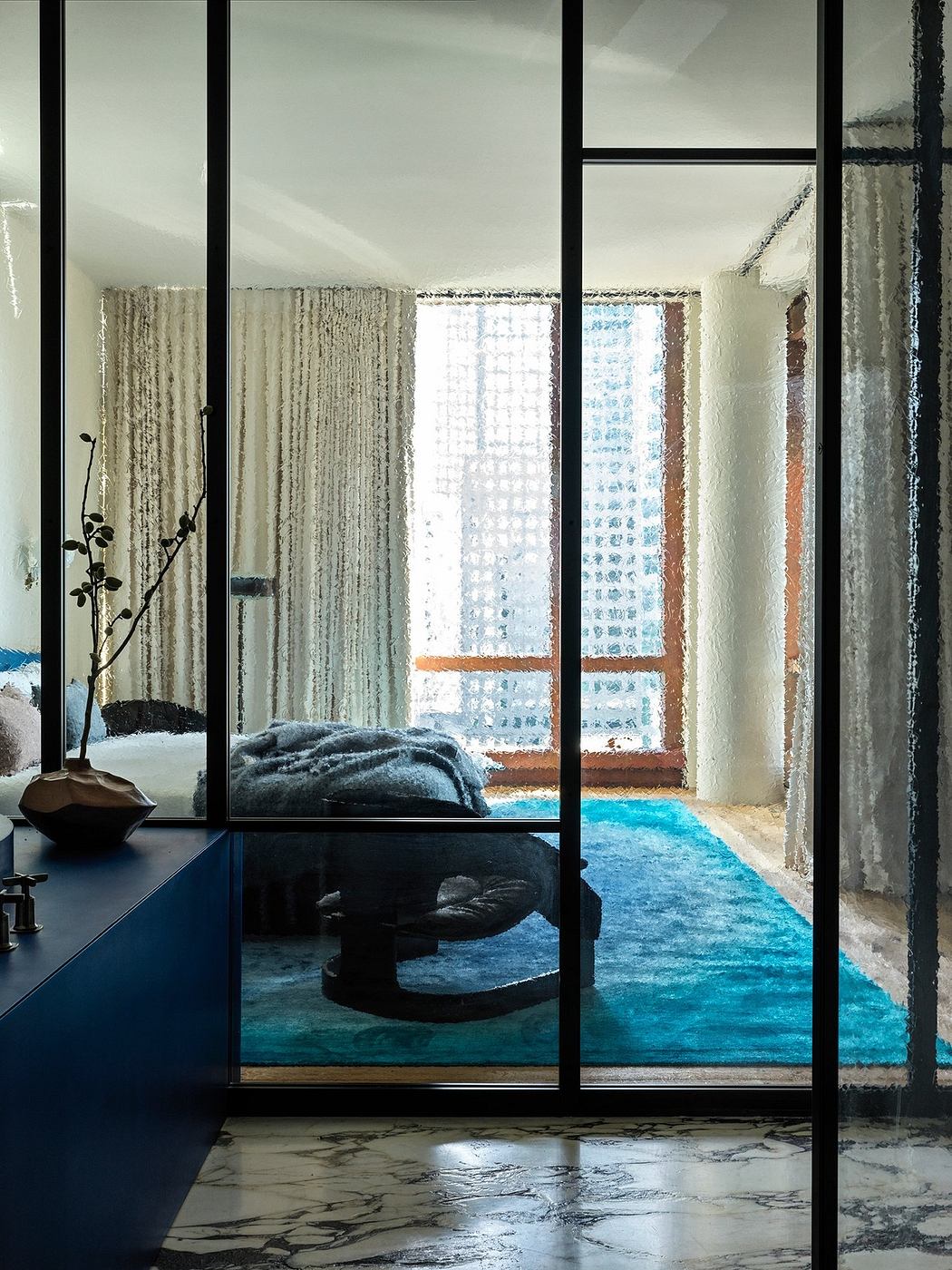 Chic bedroom with glass partition, marble floor, and vibrant blue rug