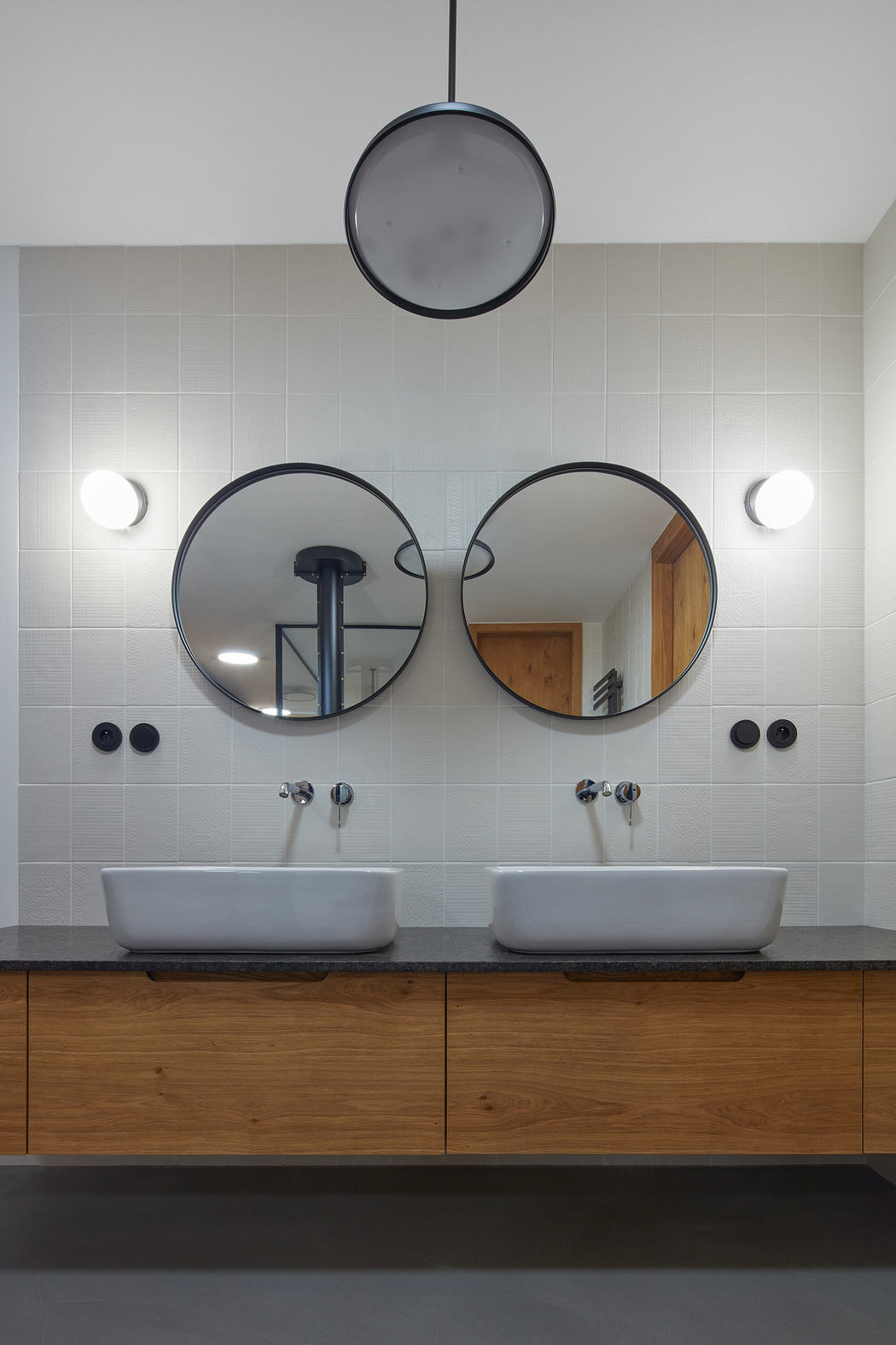 Modern bathroom with twin sinks, circular mirrors, and pendant lighting.