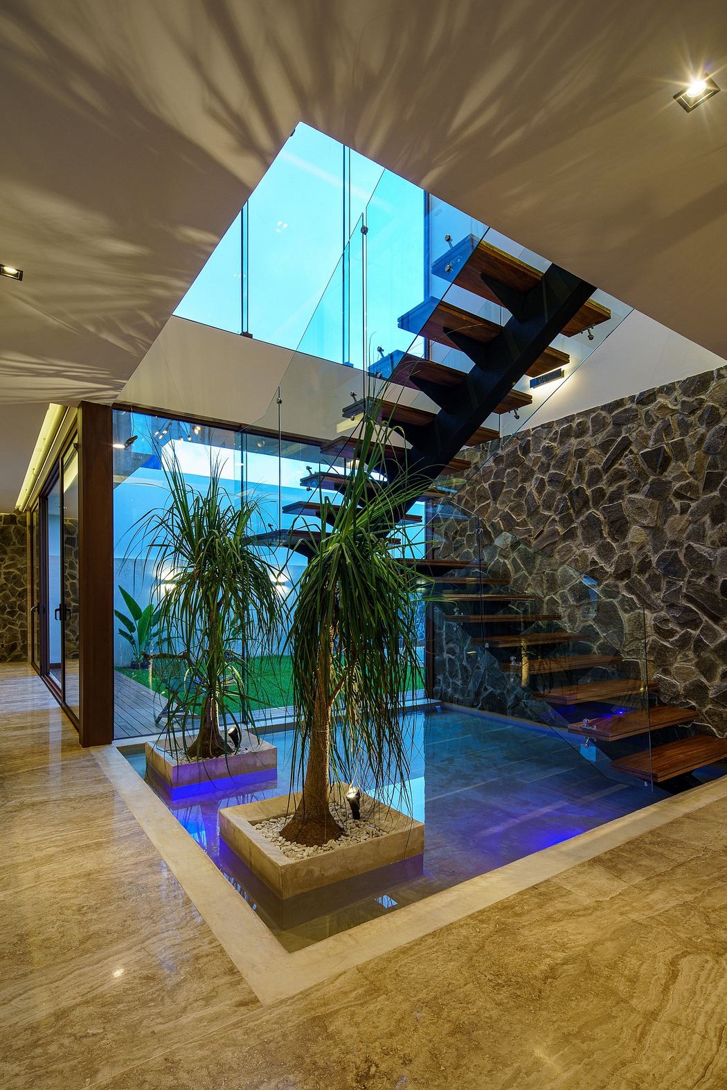 Modern interior with glass staircase, stone wall, and indoor plants.
