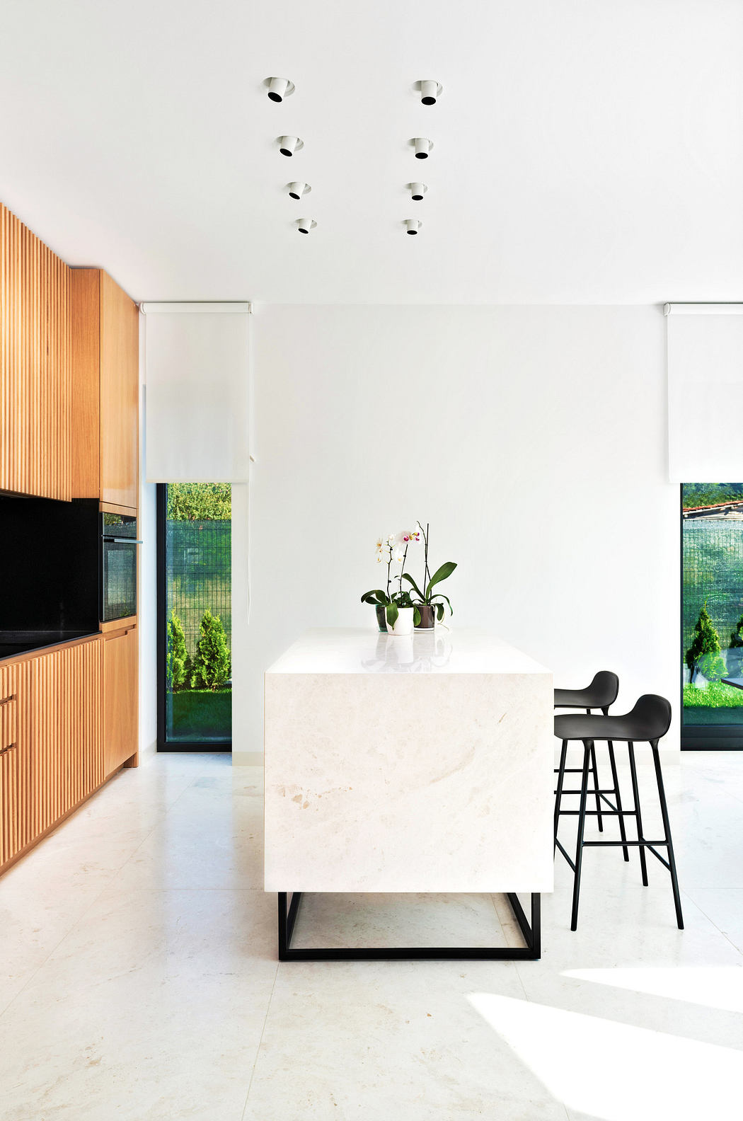 Modern kitchen with white marble island, wooden cabinets, and black stools.