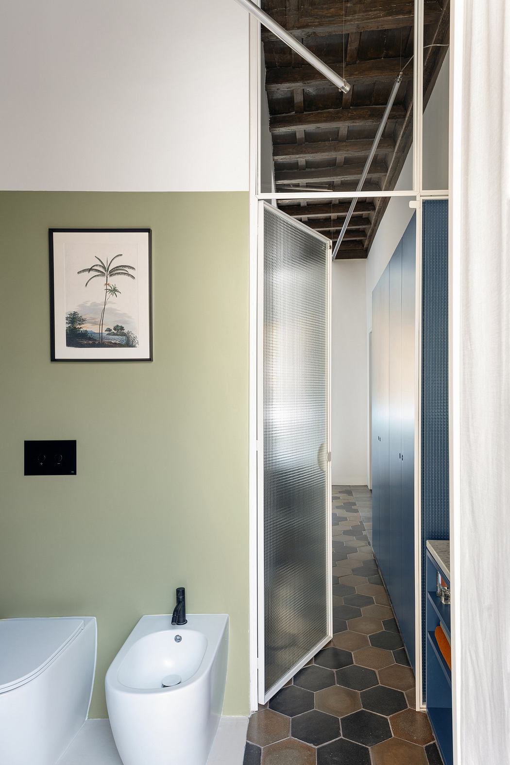 Modern bathroom with green walls, frosted glass door, and exposed ceiling beams.