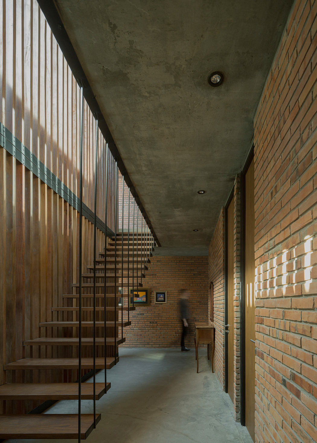 Contemporary hallway with exposed brick walls and floating wooden staircase.