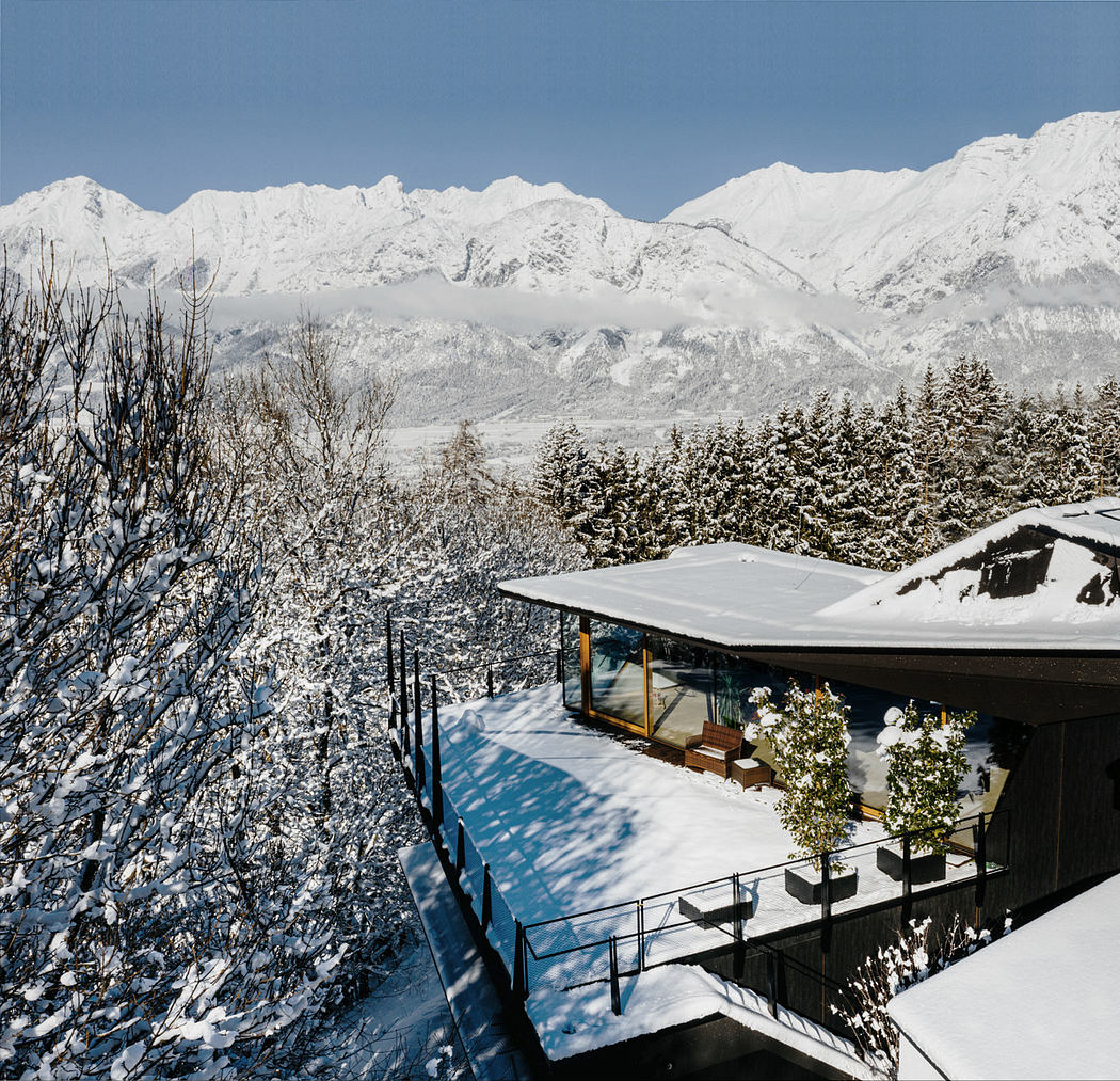Modern house with glass walls facing snowy mountains.