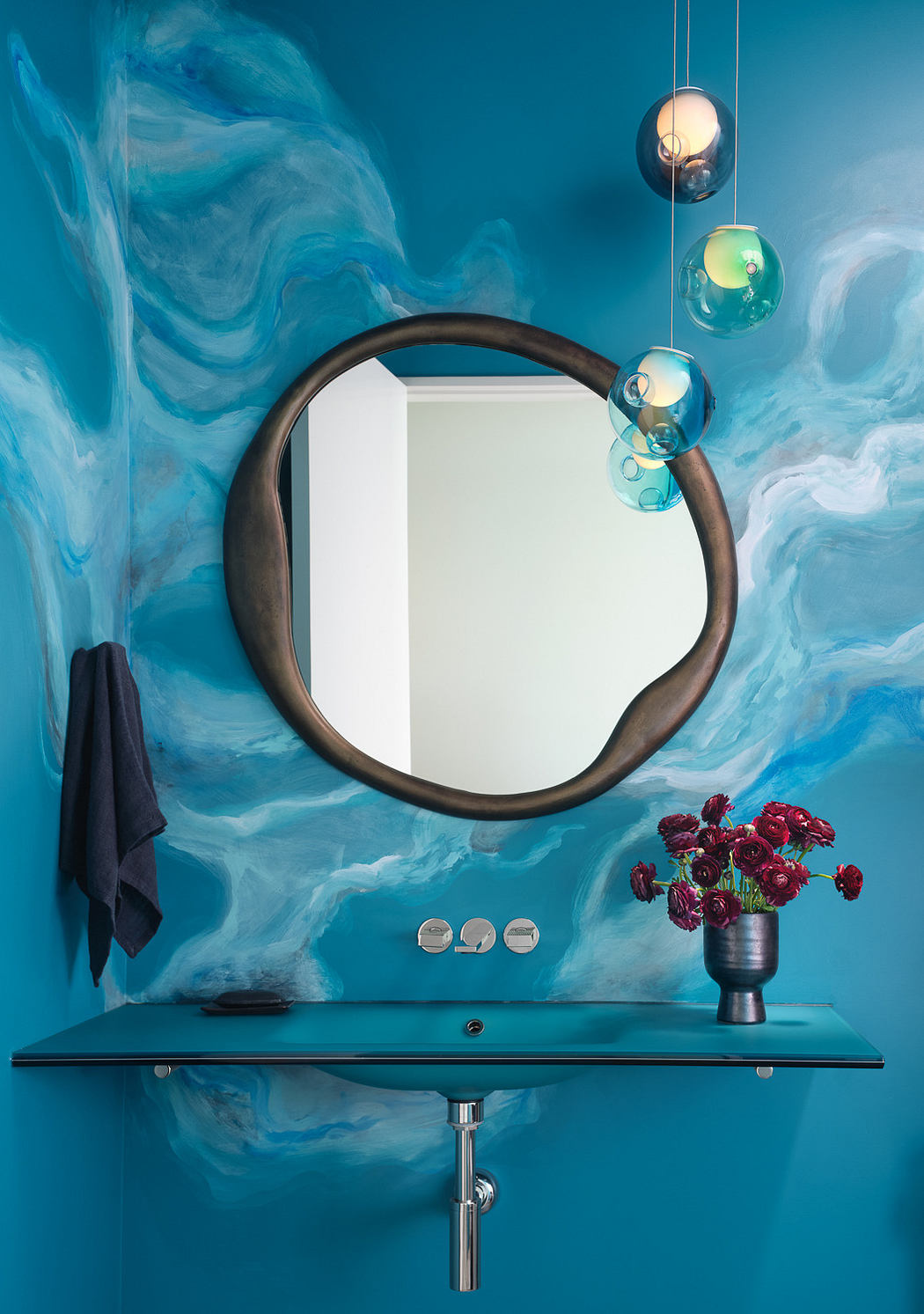 Modern bathroom with blue swirling wall pattern, round mirror, and decorative lights.