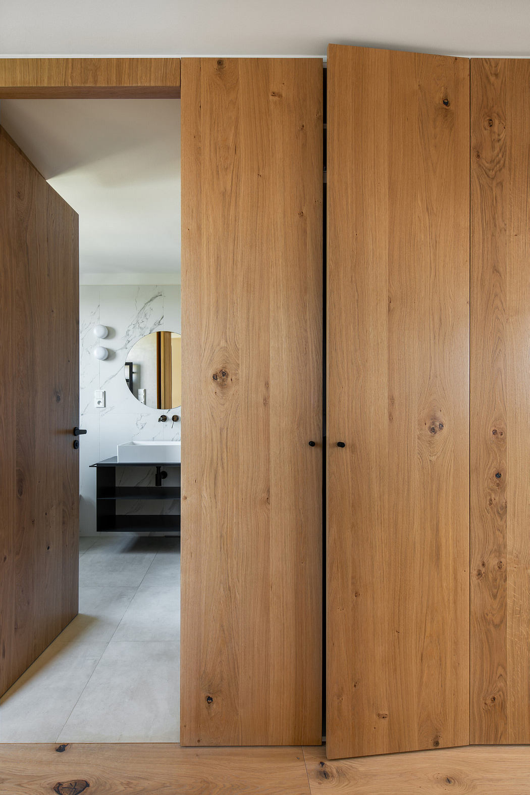 Wooden doors partially open leading to a modern bathroom interior.