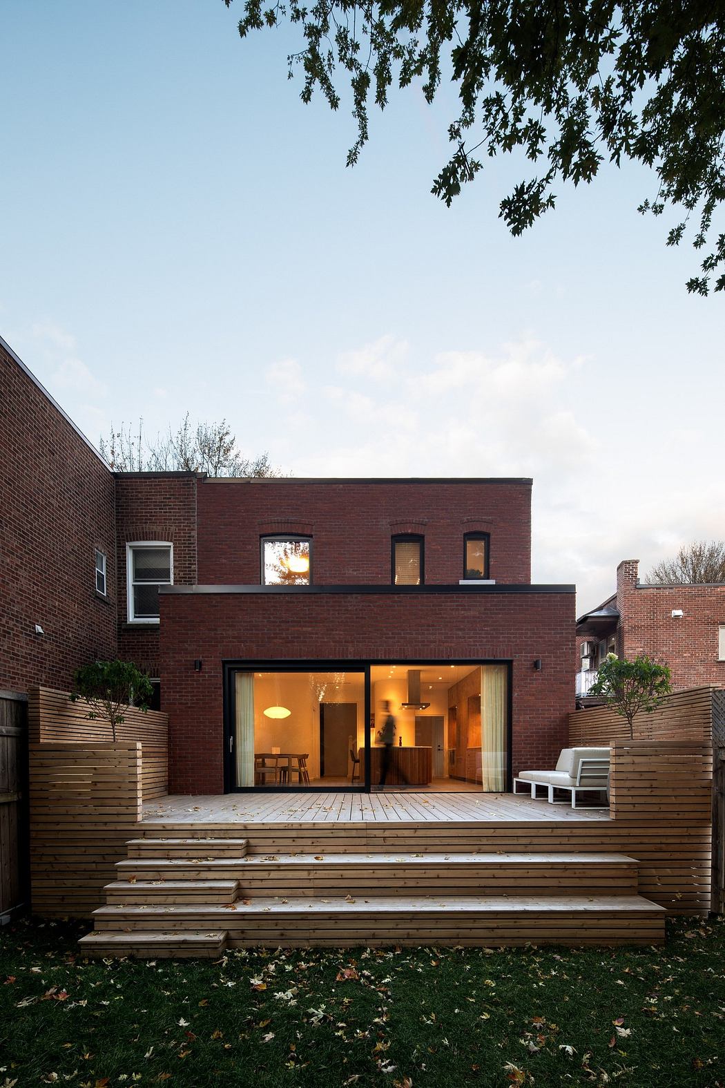 Contemporary brick house with large windows and wooden deck at dusk.