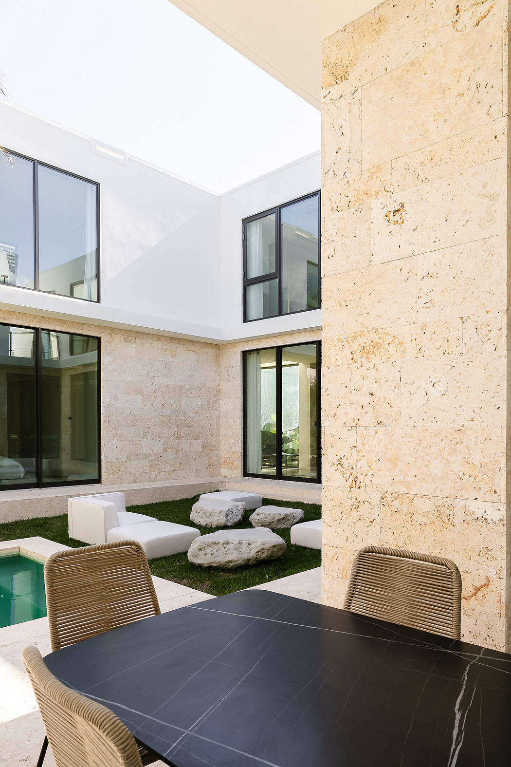 Modern courtyard with a dark table, stone wall, and a small pool.