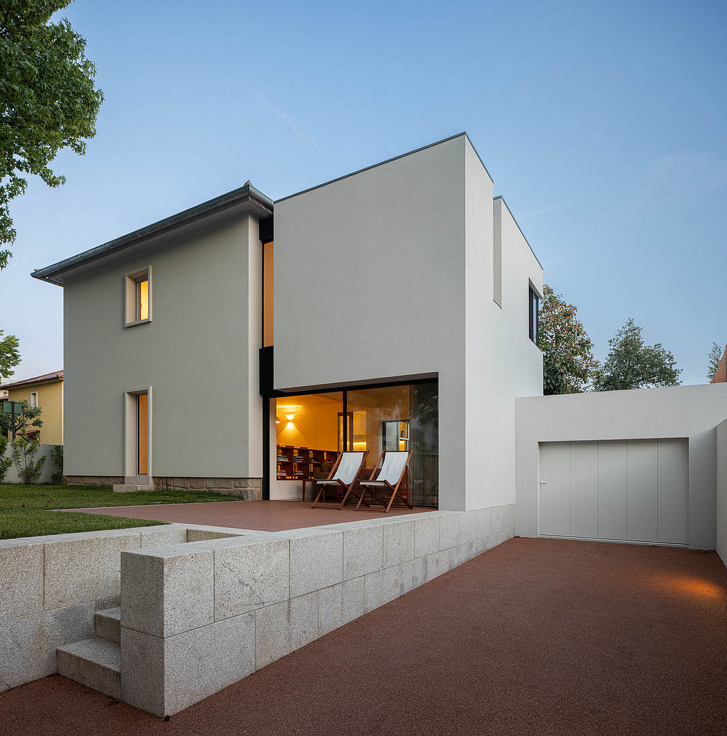 Modern house with large windows at dusk, warm interior lights visible.