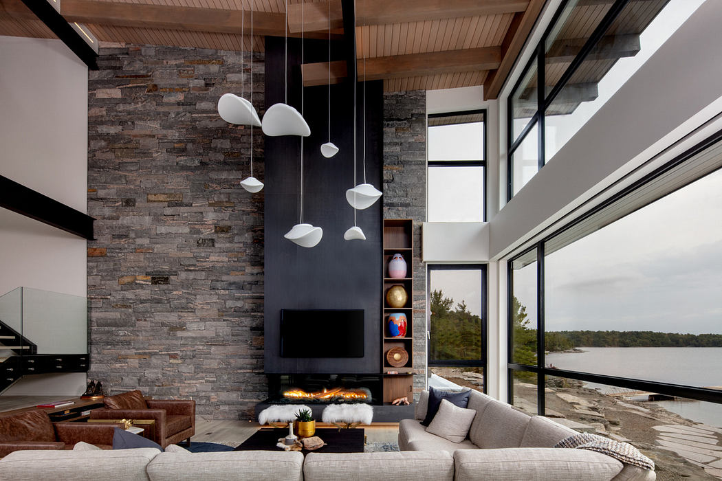 Modern living room with stone fireplace, large windows, and lake view.