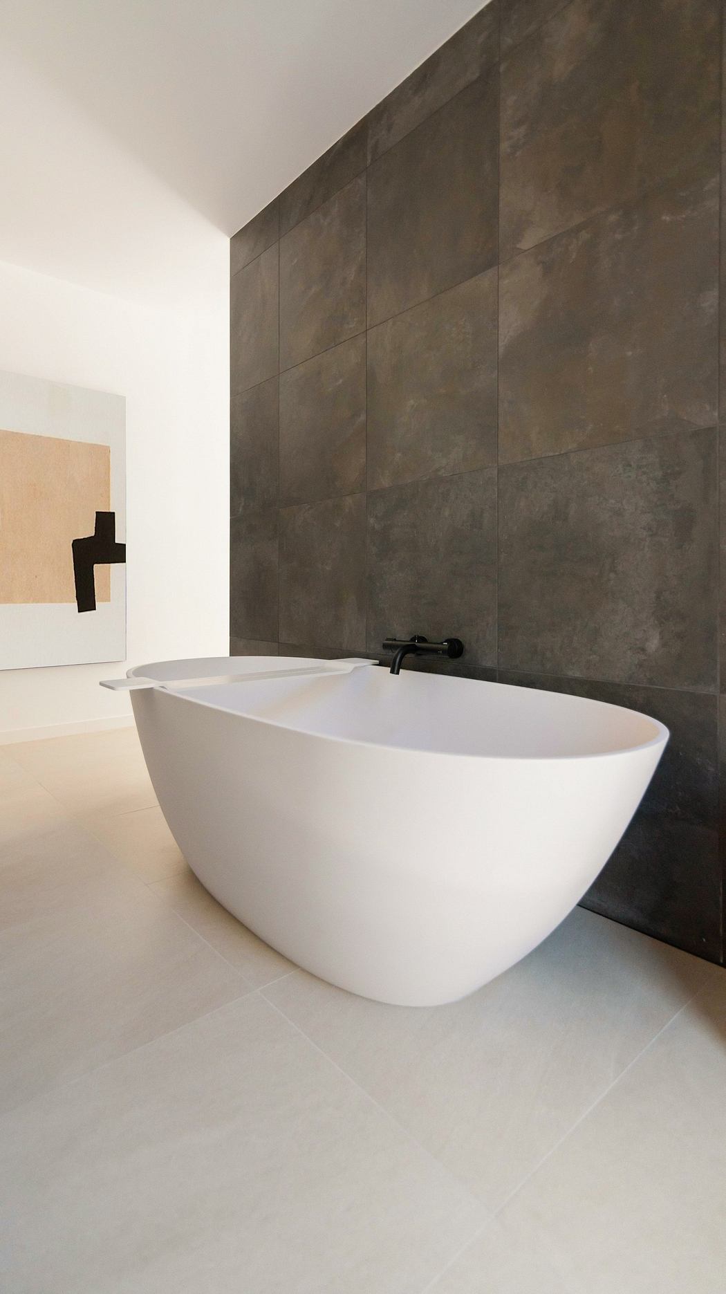 A modern bathroom with a freestanding white tub against a large dark tiled wall