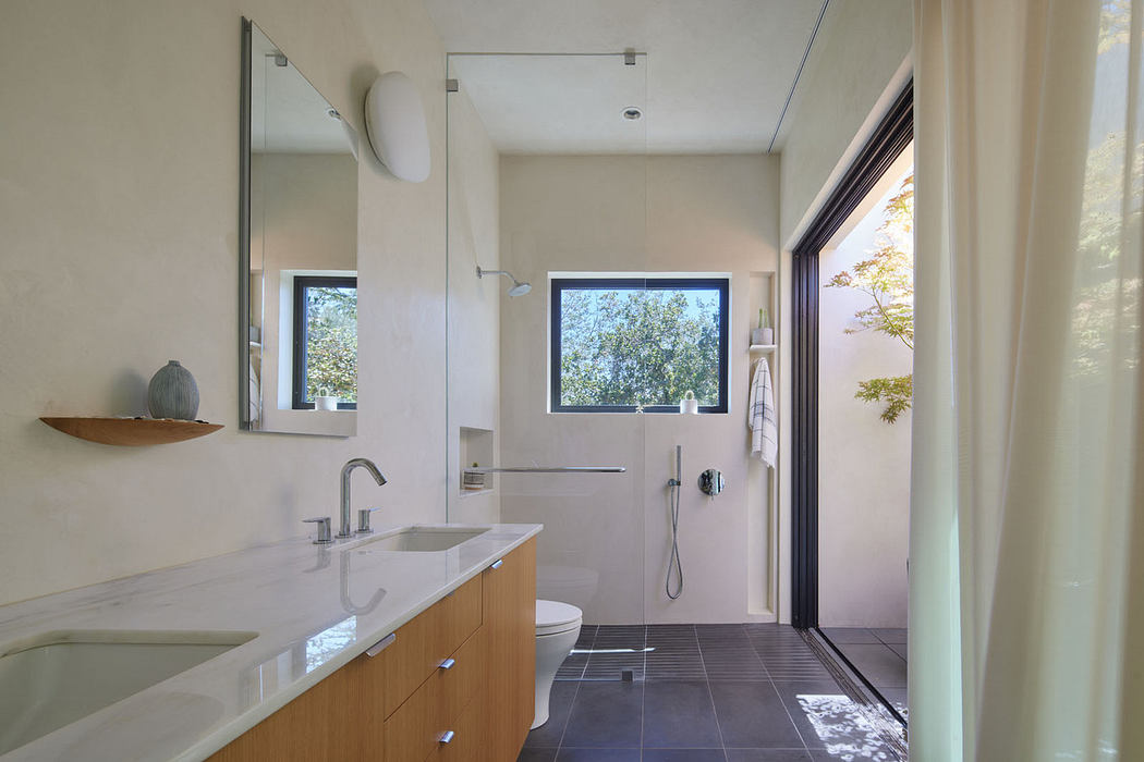 Modern bathroom with double vanity, large mirror, and open door leading outside.