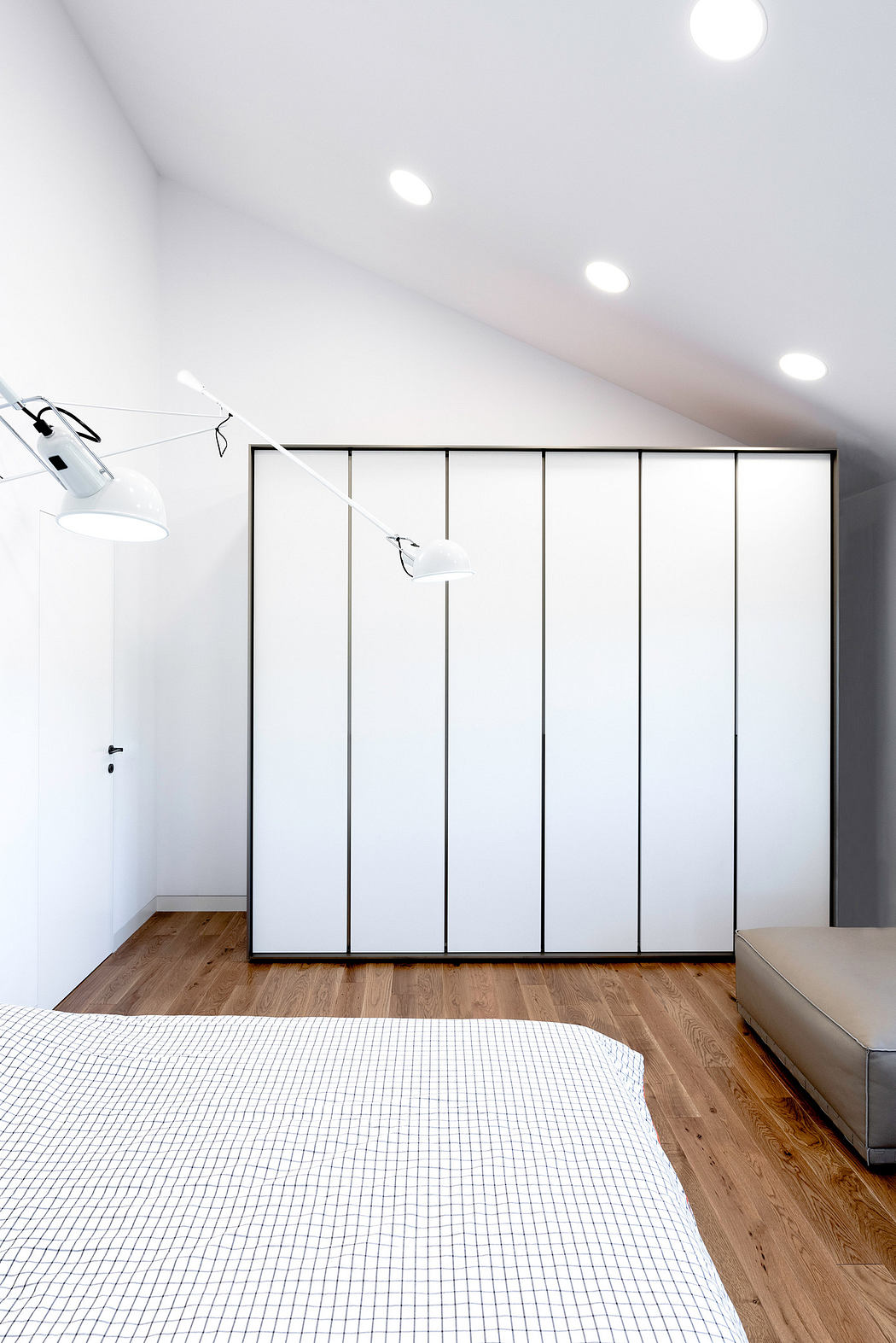 Minimalist bedroom with white walls, built-in closet, and wooden floor.
