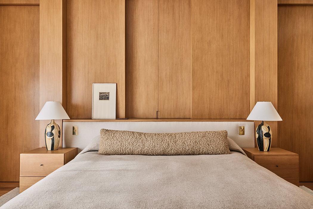 Modern bedroom with wooden panel wall, beige bedding, and matching bedside lamps.